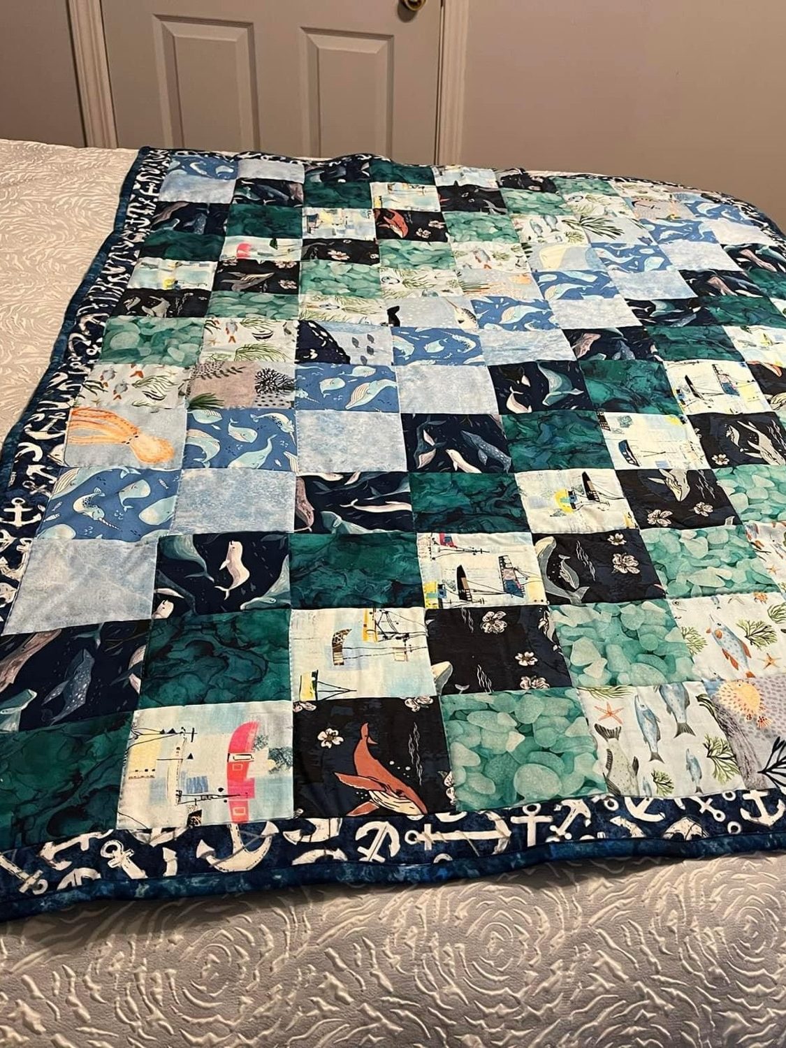 A hand-stitched quilt featuring a patchwork design with marine-themed fabrics, displayed on a bed.
